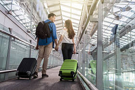 旅行者对亚裔夫妇与行李箱在机场。情人旅行和运输技术概念