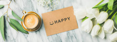 女性晨布置。白色郁金香花, 杯子咖啡并且卡片以詞愉快在輕的大理石背景下