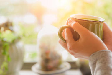 女人在早上手控股杯熱騰騰的咖啡或茶