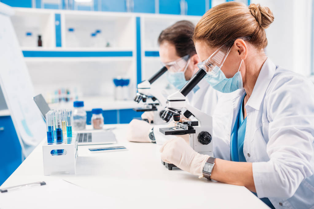 科学家在医学面具和护目镜中的选择性聚焦实验室中的董事看显微镜