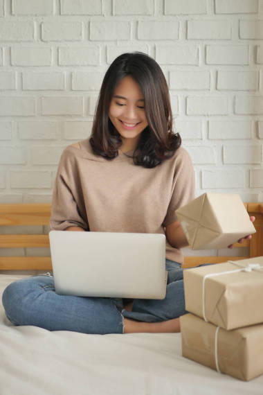 快乐的妇女与计算机和产品包裹盒在家