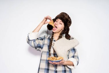一個(gè)年輕的俄羅斯女孩在毛皮帽子吃熱可口的煎餅, 慶祝 Shrovetide