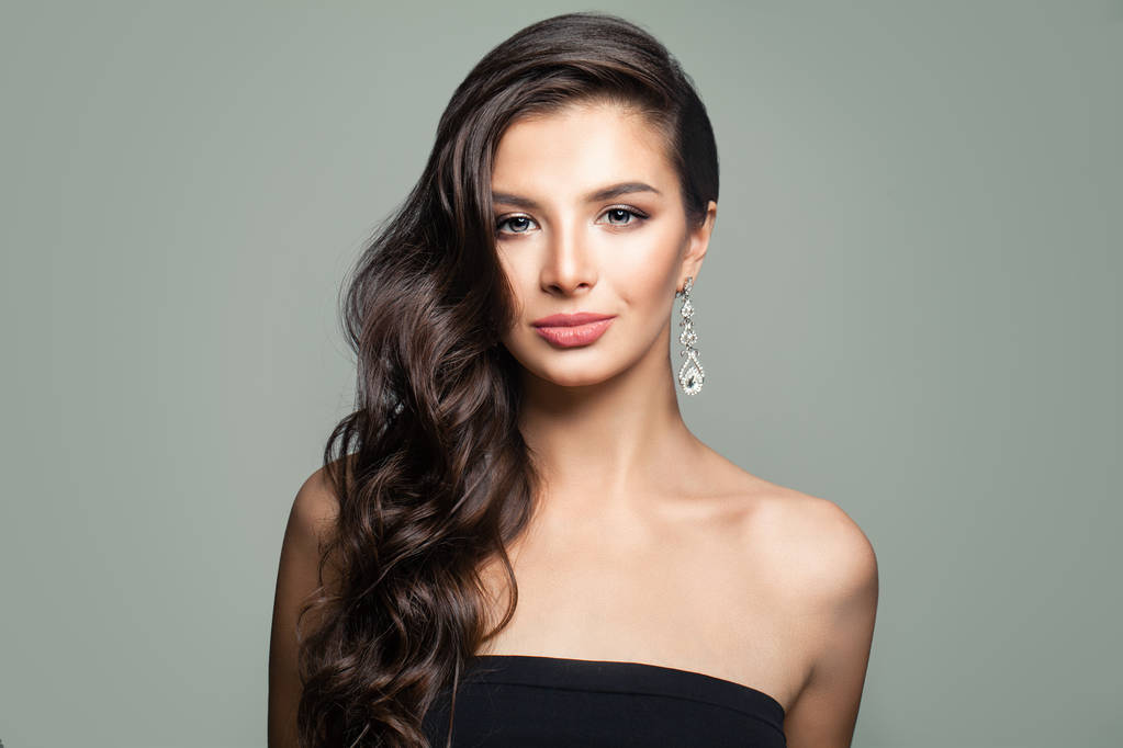 美丽的黑发女人,用长长的卷发,在灰色的背景上 美丽的黑发女人,用长长的卷发,在灰色的背景上