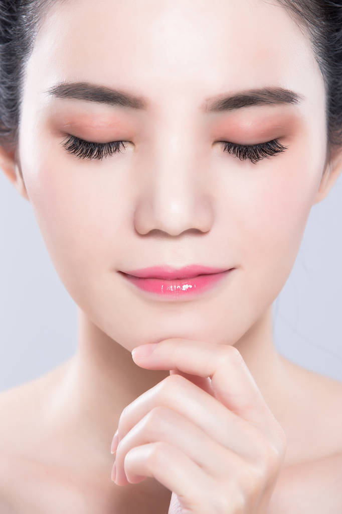 闭着眼睛的女人在灰色背景上抚摸下巴