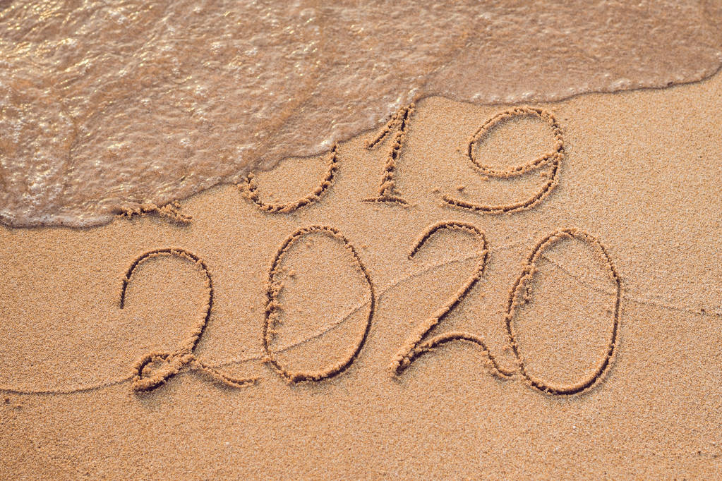 新年2020是未来概念-题字2019和2020沙滩沙子, 波浪几乎覆盖数字2019