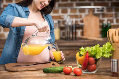在廚房里把橙汁倒進(jìn)玻璃杯的微笑懷孕婦女的鏡頭