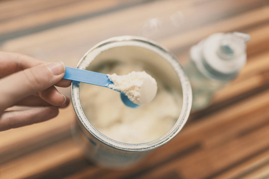 婴儿和蓝色勺子的粉末牛奶在轻的背景特写