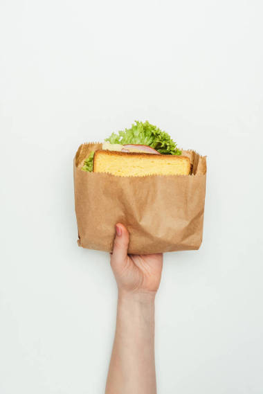 白色纸袋中夹三明治妇女的裁剪图像