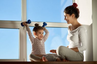 小女孩高興地舉起一個(gè)啞鈴和微笑, 炫耀他的成就給他的母親