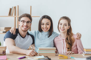 年輕的微笑的學(xué)生坐在桌與書