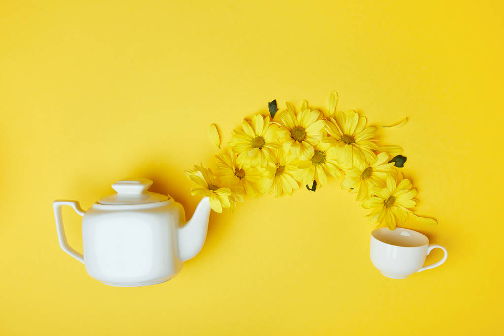 黄色菊花从白壶倒入杯中图片