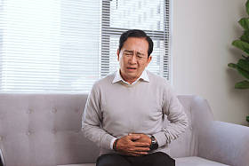 坐在沙发上的亚洲老人胃痛 照片