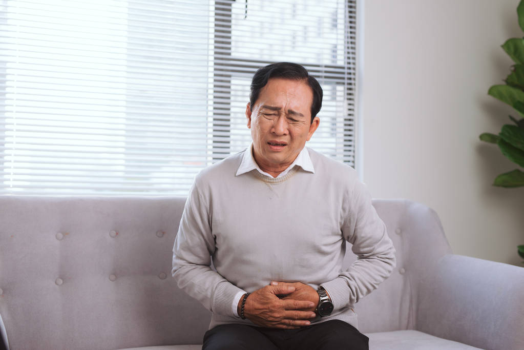 坐在沙发上的亚洲老人胃痛 照片