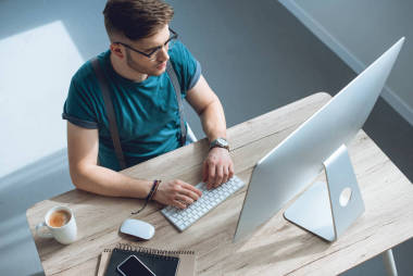 眼鏡上的年輕人在鍵盤上打字和使用臺式計算機的開銷視圖