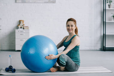 美麗的懷孕婦女坐在瑜伽墊與健身球在客廳