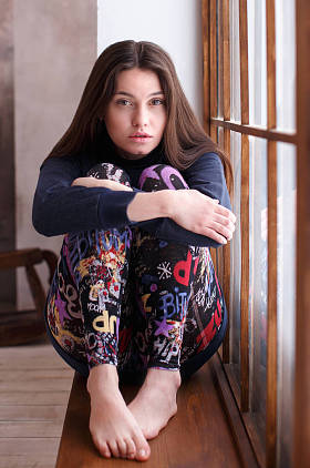 棕色头发的女孩抱着她的膝盖, 坐在窗台上放松  