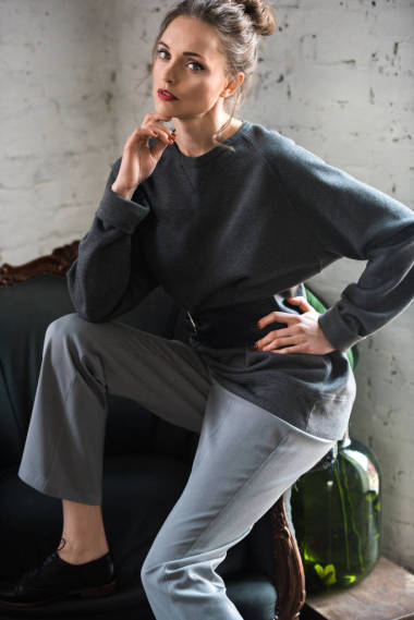 漂亮的年輕女子在時髦的跳線與皮帶坐在扶手椅上, 看著相機