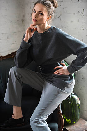 漂亮的年轻女子在时髦的跳线与皮带坐在扶手椅上, 看着相机