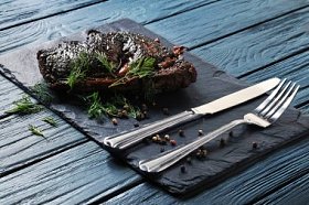 烤肉用绿色莳萝, 胡椒, 银叉子和刀子在板和蓝色木背景