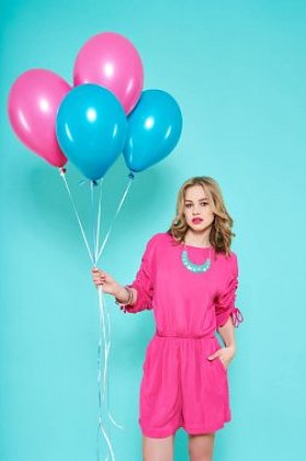 华丽时髦的年轻女子在派对服装手持一束气球淡蓝色背景上的生日派对概念