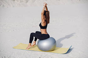 美丽的健身女孩做伸展运动与合适的球在海滩上。体育和健康的生活方式概念。做普拉提锻炼的年轻妇女