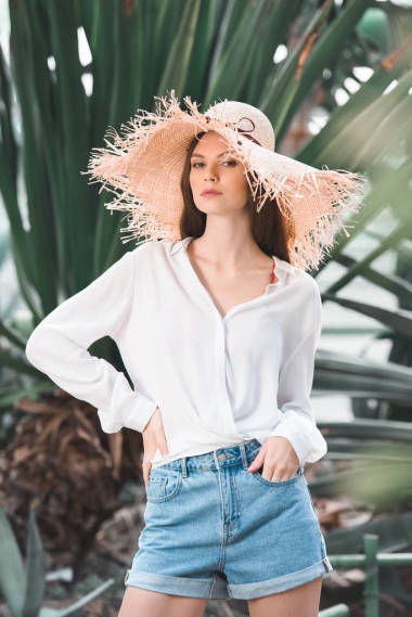 美麗的女人在夏天的上衣和草帽擺在熱帶花園