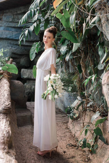 美麗的新娘擺在白色禮服與婚禮花束在熱帶花園