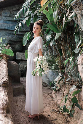 美丽的新娘摆在白色礼服与婚礼花束在热带花园
