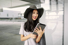 美丽时尚的亚洲妇女与平板摆在现代建筑附近