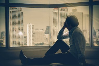 沮丧的人坐在手上的室内摩天大楼与低光环境在城市景观背景的窗口, 戏剧性的概念