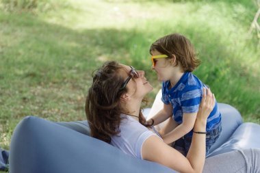 春天, 媽媽和她的孩子正在一棵樹下的充氣沙發(fā)上玩耍