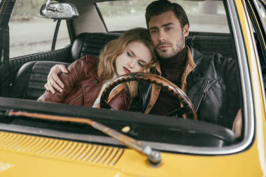 时尚体贴的年轻夫妇在皮革夹克坐在一起老式汽车