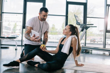 男性私人教練顯示數(shù)字片運(yùn)動員坐在健身墊在健身房