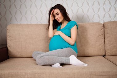 懷孕婦女的抑郁癥。一個年輕的孕婦坐在沙發(fā)上哭著回家