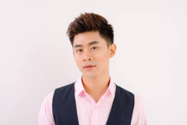 英俊的亞洲男子站在粉紅色的襯衫, 在灰色的背景下擺出笑臉