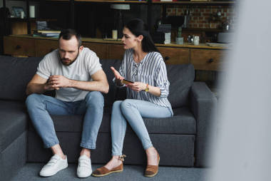 悲傷的年輕人坐在沙發(fā)上, 看著他的妻子喊他和持有信用卡