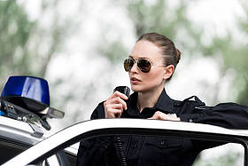 有吸引力的女警察在警车附近讲话由收音机设置
