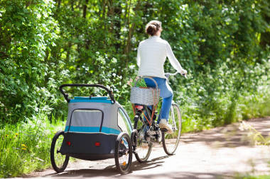 母親在自行車(chē)與嬰兒自行車(chē)拖車(chē)在公園