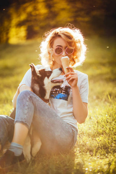 戴眼镜的时髦女孩在公园炎热的天气里吃冰淇淋, 手里拿着哈士奇
