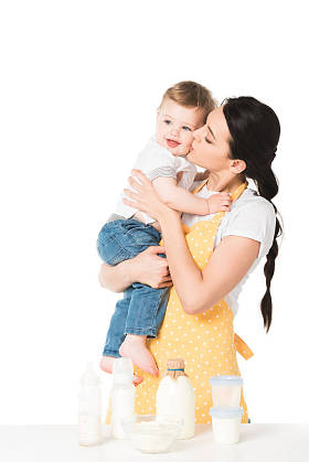 母亲亲吻男孩在面颊在桌与孩子食物在白色背景被隔绝了