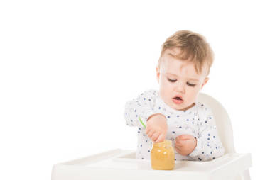 小男孩吃泥從罐子和坐在高腳隔絕在白色背景上