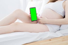 床上挂着绿色屏幕的孕妇