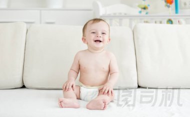 快樂的笑孩子在尿布坐在沙發(fā)上, 看著相機