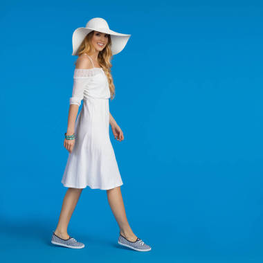 穿著白色夏季禮服, 運動鞋和太陽帽散步的女人。側面視圖