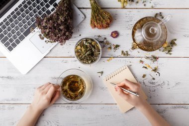 各種茶葉的頭頂景色。用各式各樣的草藥調(diào)味, 一個(gè)蘋果, 玫瑰與茶壺和茶杯在鄉(xiāng)間餐桌上