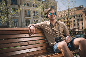 戴着照相机, 耳机和智能手机坐在长椅上的年轻人