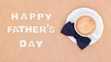 父親節(jié)快樂的背景。杯咖啡和黑弓領(lǐng)帶在棕色背景平躺。父親日靜物