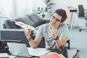 兴奋的学生与膝上型电脑在家做家庭作