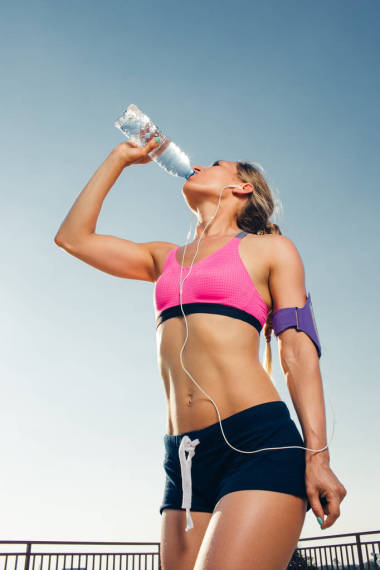 智能手机耳机中年轻运动员的低角度看屋顶上瓶子的饮水