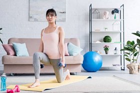 漂亮的年轻女人做一条腿蹲在家里哑铃